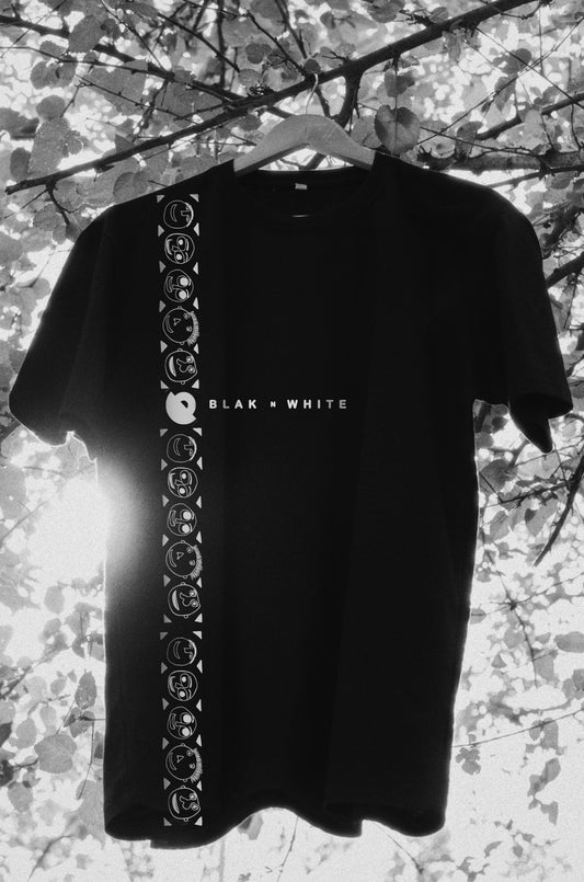 Oversized black t-shirt with short sleeves and round neckline, featuring a design with what appears to be floral patterns or moody illustrations along the front and sleeves, hung on a tree branch with a blurred background.